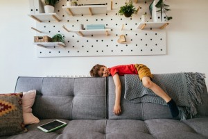 Photo of a little boy who is being bored, lying down on the sofa in his living room.