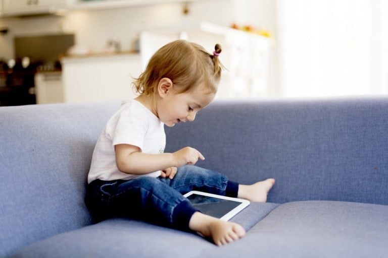 Cute little girl sitting on the couch using a digital tablet.