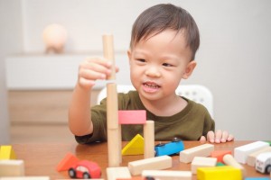 Cute little Asian toddler boy child having fun playing with wooden building block toys.