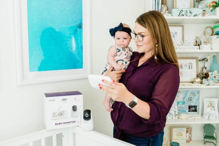 Mom holding her daughter as she is looks at the VAVA baby monitor.