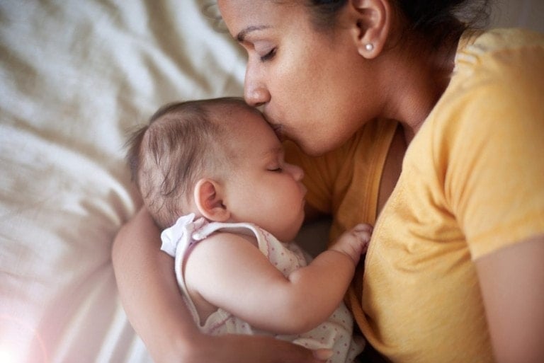 An adorable baby girl sleeping peacefully in her mother's arms at home.