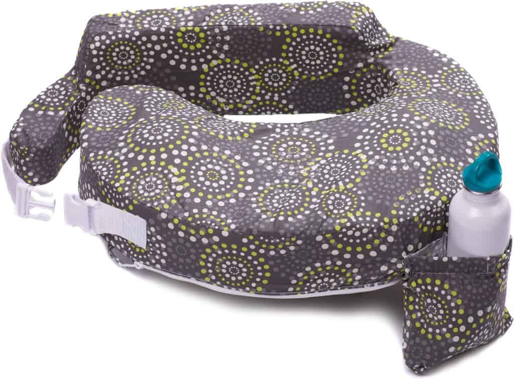 A U-shaped nursing pillow featuring a grey cover with white and green circular patterns—essential for postpartum recovery. The pillow includes a white adjustable strap with a buckle and an attached small pouch holding a white bottle with a blue cap.