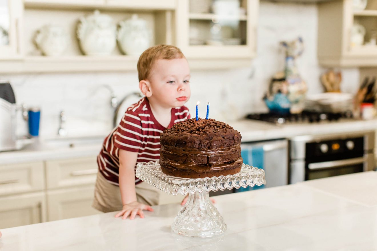 Toddler boy blowing out his birthday candles on his chocolate birthday cake.