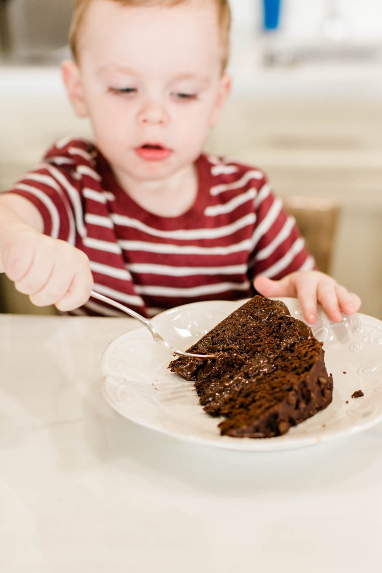 Toddler boy using a fork to take a piece of his chocolate cake.