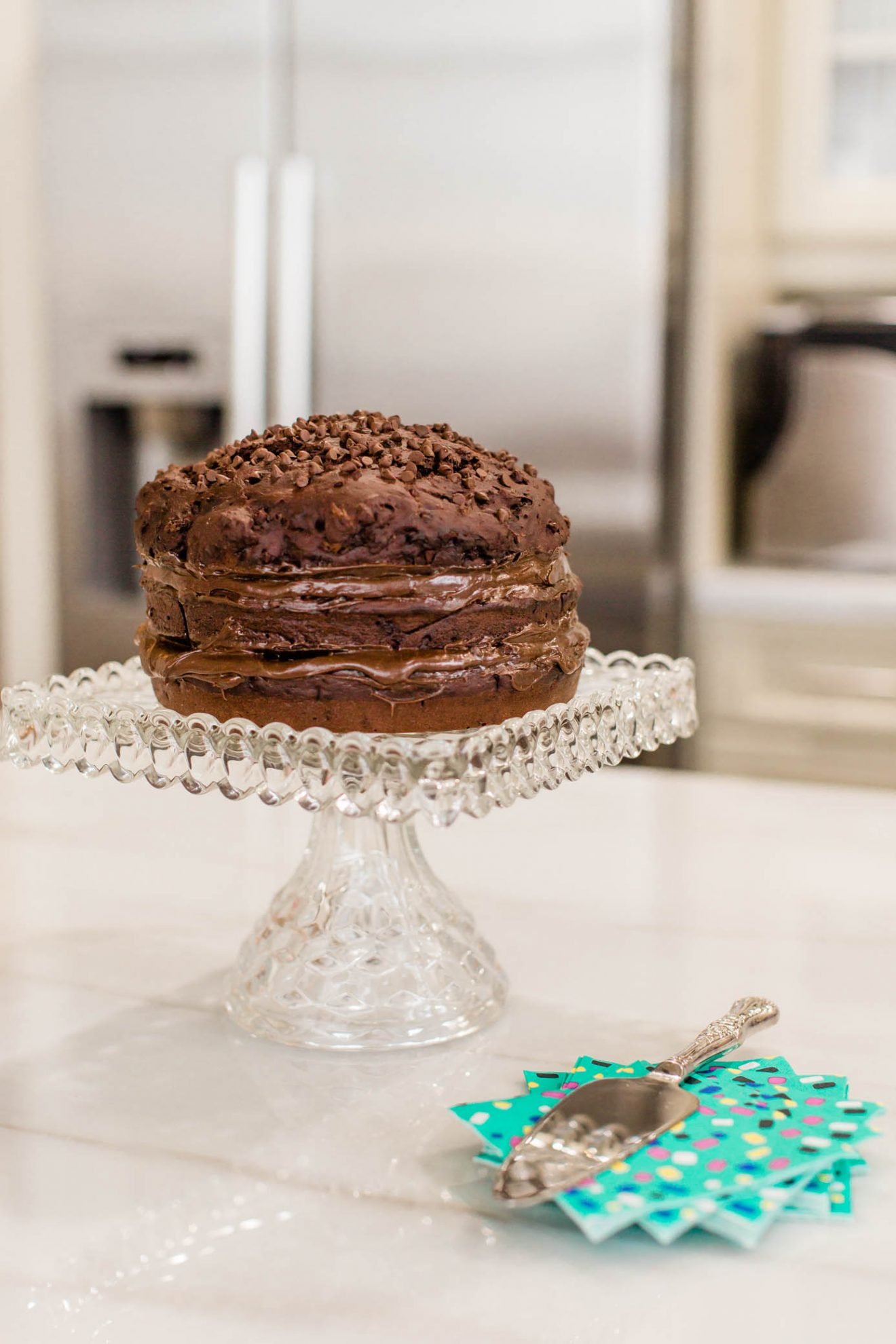 Chocolate cake on a cake stand in the kitchen with a serving knife and napkins.