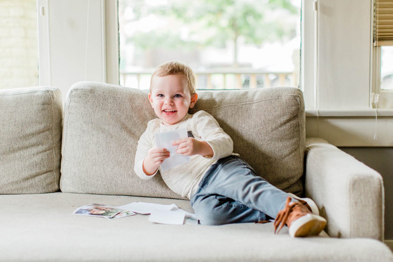 Toddler boy sitting on a couch looking at pictures.