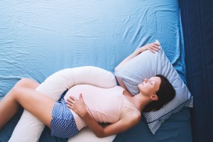 Beautiful pregnant woman relaxing or sleeping with tummy supporting pillow at bed. Young mother waiting of a baby. Concept of pregnancy, maternity, health care, gynecology, medicine.