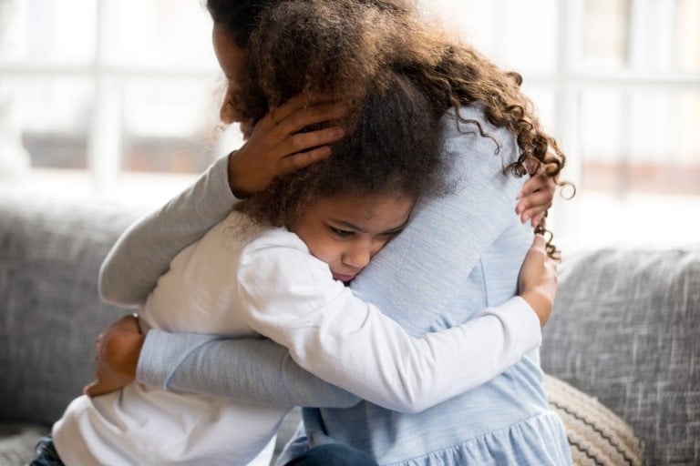 Black African mother embrace little preschool frustrated kid sitting on couch together at home. American loving mother supports disappointed daughter sympathizing, making peace after scolding concept.