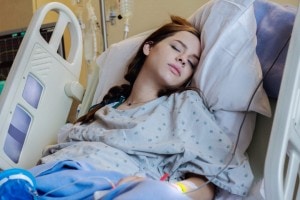 A woman with long brown hair lies in a hospital bed, wearing a hospital gown and resting with her eyes closed. She has a nasal cannula for oxygen and an IV line attached to her arm, as she undergoes labor induction. The room has medical equipment visible in the background.