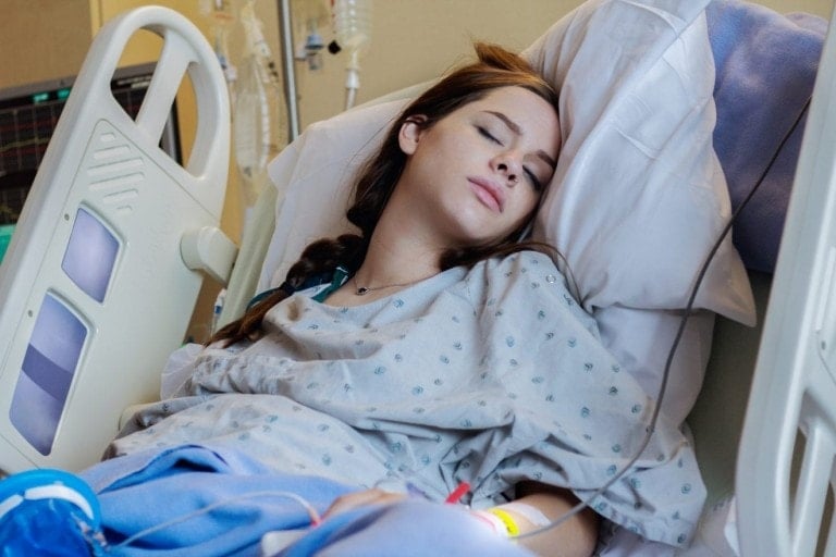Caucasian teenage girl has her eyes closed as she is lying in a hospital bed during childbirth. Young pregnant mother is preparing to have her first baby.