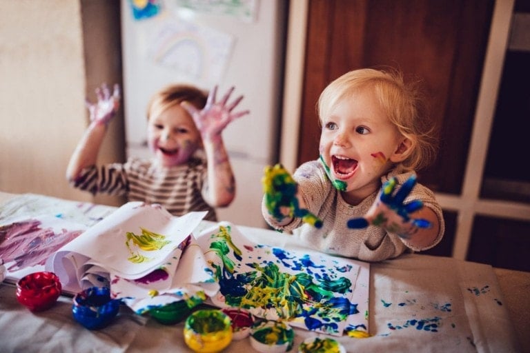 Happy little girls with dirty hands and faces having fun being creative with finger painting.