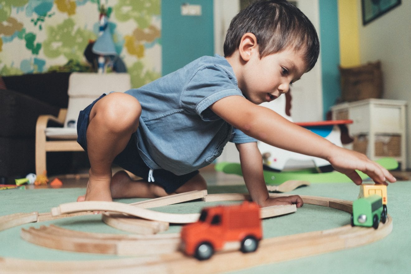 Cute little boy playing with wooden train on the floor at home.