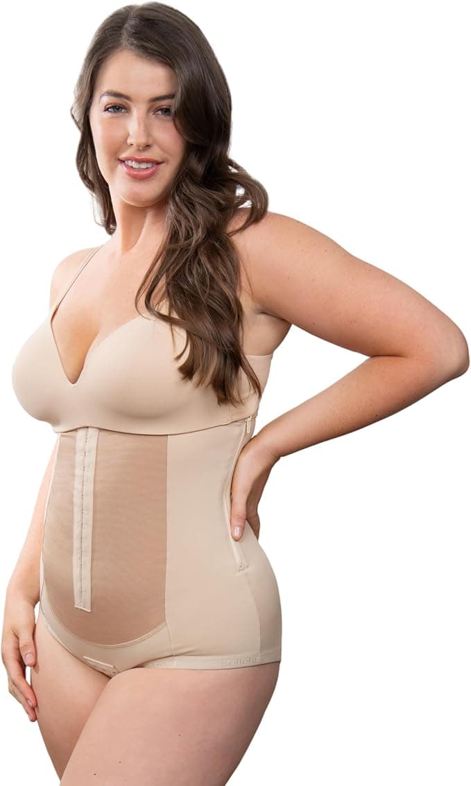 A woman in a beige shapewear bodysuit, ideal for c-section recovery must-haves, stands smiling. The bodysuit features thin straps and extends from the chest to the upper thighs. Her long brown hair cascades as she poses confidently with one hand on her hip against a white backdrop.