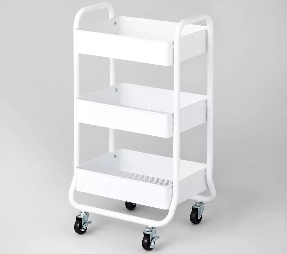 A white metal utility cart with three rectangular shelves and four black caster wheels is perfect for organizing c-section recovery must-haves. The design features curved handles at the top, and its open structure ensures easy access to all essentials without any side or back enclosures.