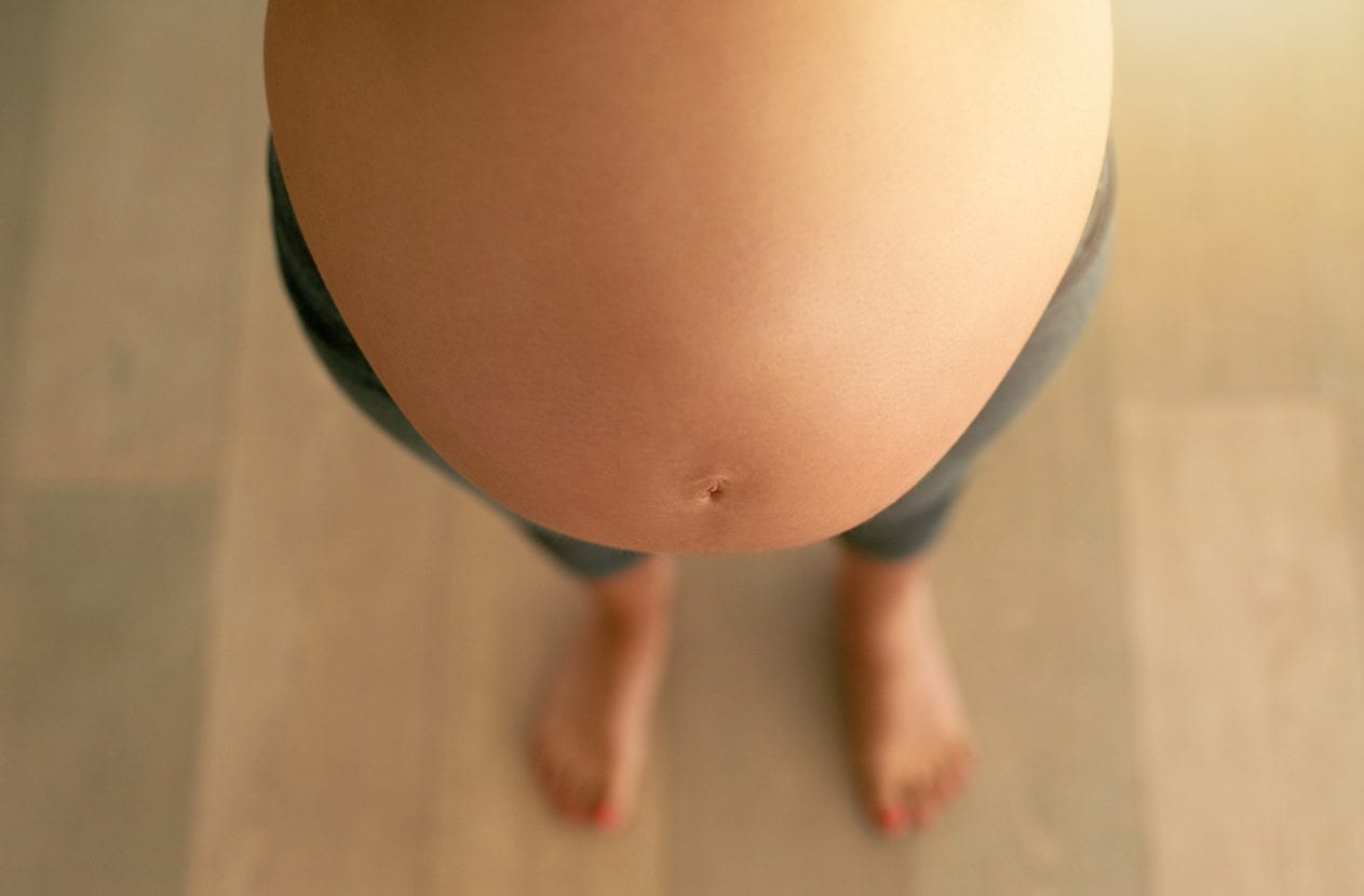 Looking down on woman's pregnant belly and wearing maternity leggings.