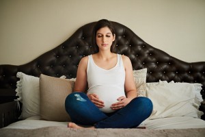 Pregnant woman meditating on her bed while cradling her belly.