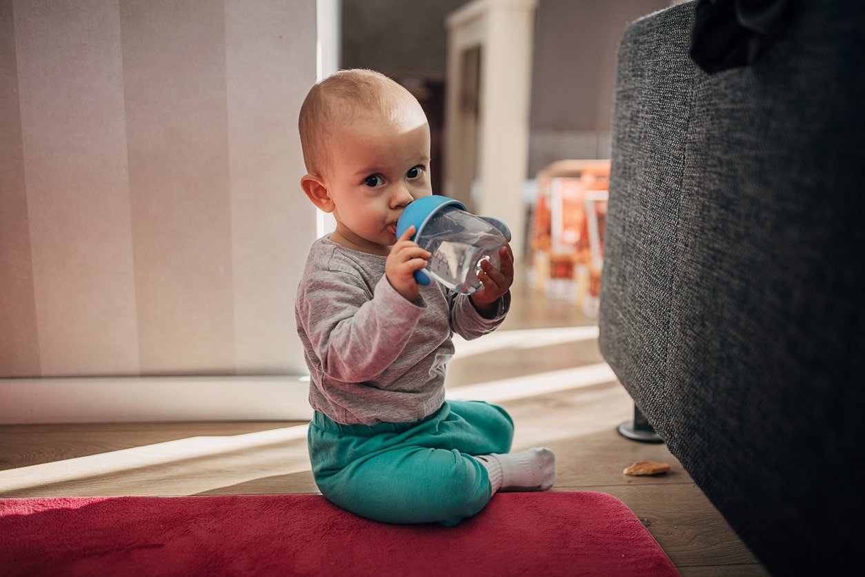 Adorable baby boy sitting on the floor and drinking water from his bottle.