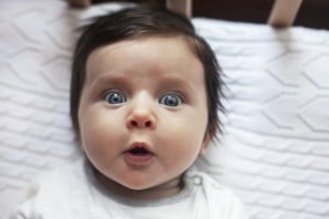 Surprised funny cute baby with blues eyes close portrait, lying in bed