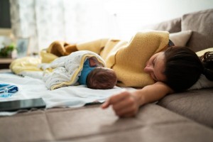 Mother and newborn baby boy sleeping, lying on bed together during a day, covered with blankets