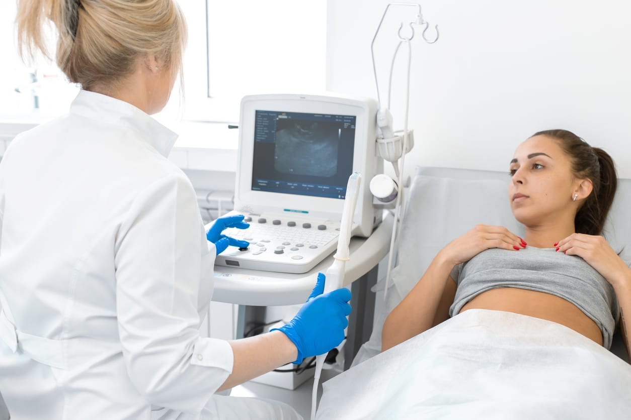 A gynecologist sets up an ultrasound machine to diagnose a patient who is lying on a couch. A transvaginal ultrasound scanner of the internal organs of the pelvis. Female health concept.