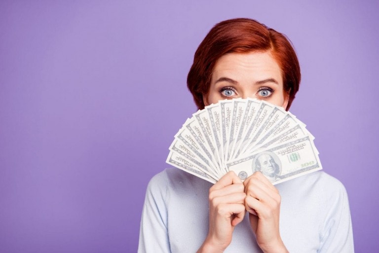 Close up portrait of a woman showing a bunch of money in front of her face with satisfied look.
