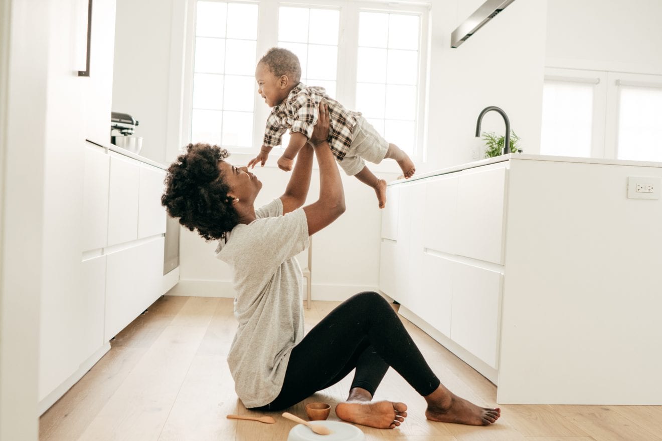 A minimalist mom sitting on the kitchen floor playing with her son.