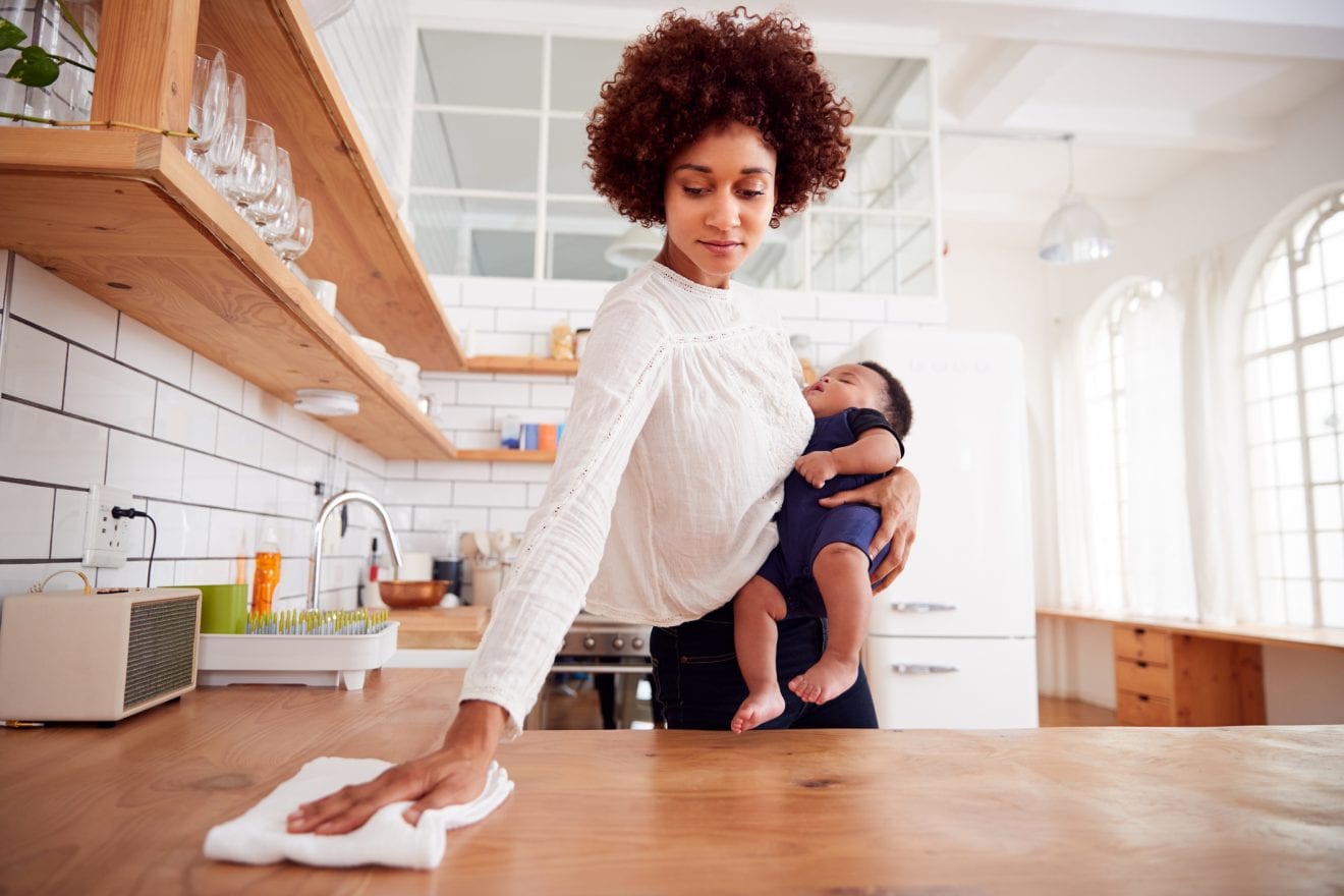 Multi-Tasking Mother Holds Sleeping Baby Son And Cleans In Kitchen
