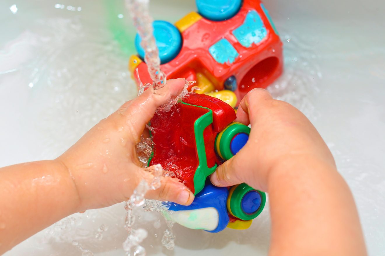 A little kid washing the toy trucks in the sink.