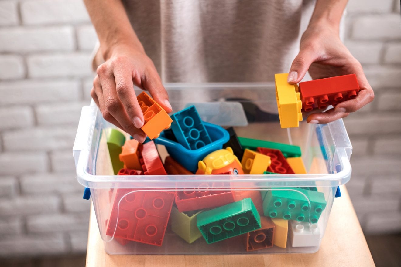 Woman's hands putting colored blocks into plastic box.