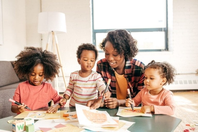 A mom with her toddlers creating at the table with paper and markers.