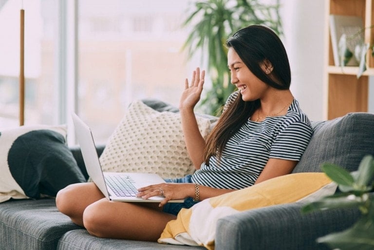 Shot of a young woman using a laptop and waving on the sofa at home