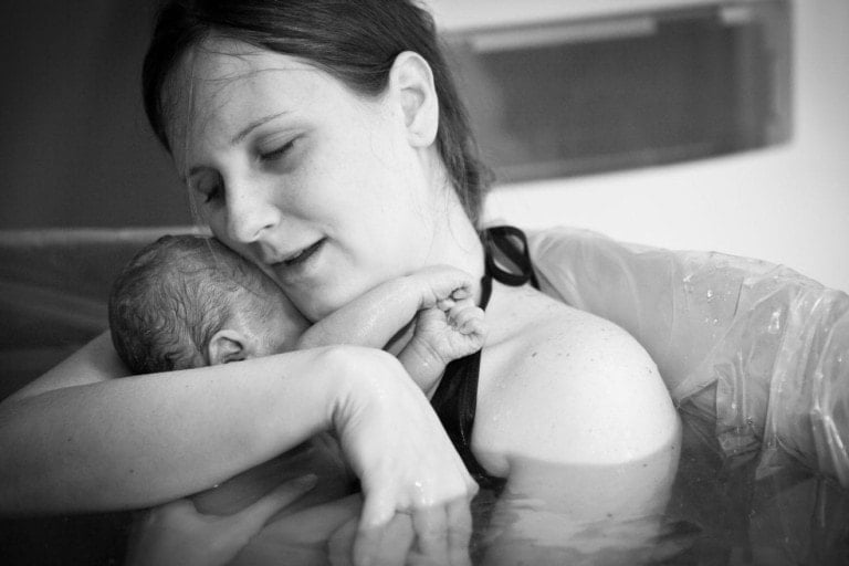 Black and white image of a young mother embracing her newborn son after giving birth at home.