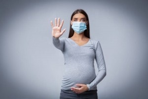 Pregnant Lady In Medical Face Mask Gesturing Stop Posing Over Gray Background In Studio