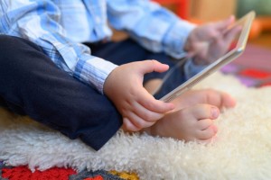 A little boy sitting on the floor playing on an iPad or smart tablet.