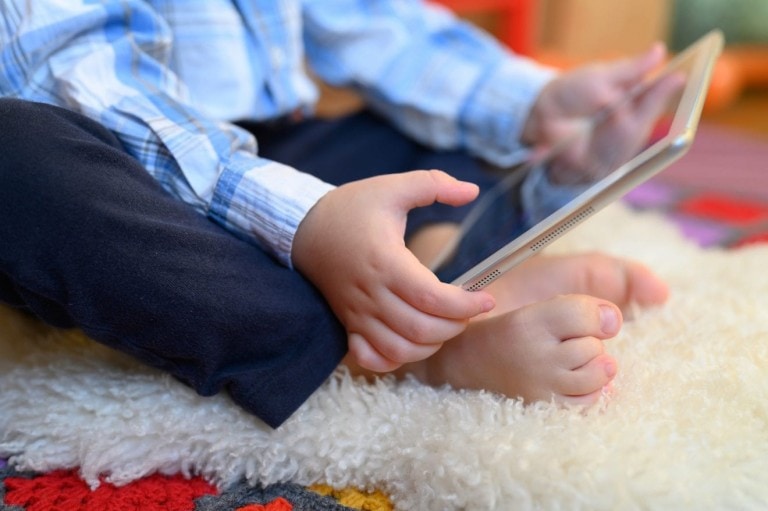 A little boy sitting on the floor playing on an iPad or smart tablet.