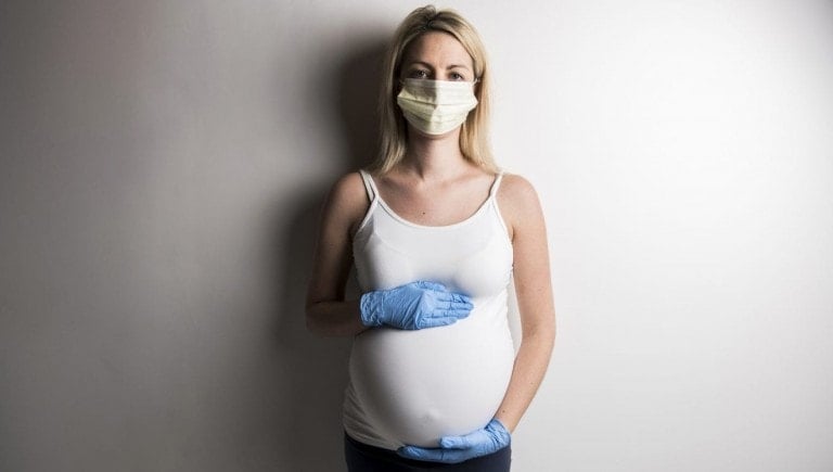 A pregnant woman in protective mask against infectious diseases and flu showing stop gesture with glove. Health care concept.