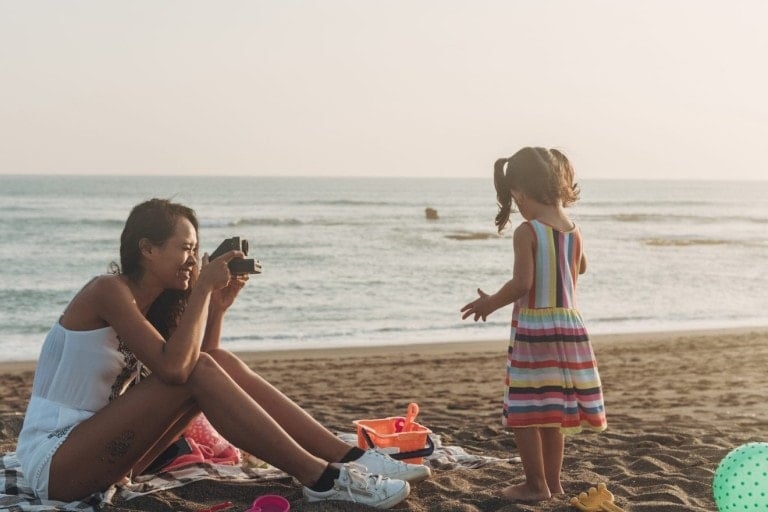 Mother photographing little daughter at the beach with instant camera.