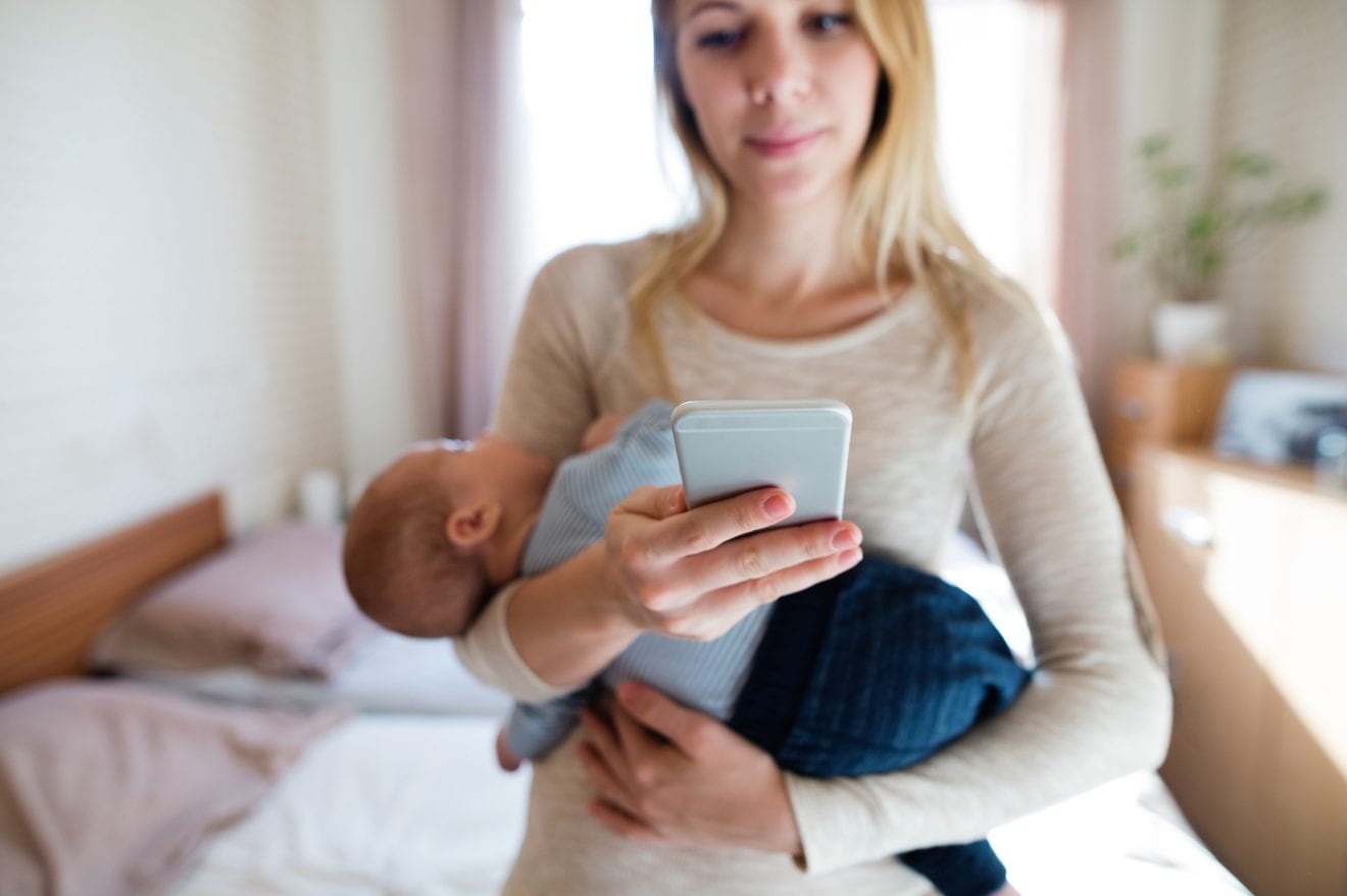 Mother with baby son in her arms and smartphone, texting