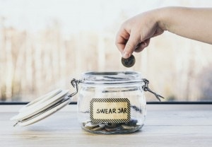 Hand putting in a coin into a swear jar.