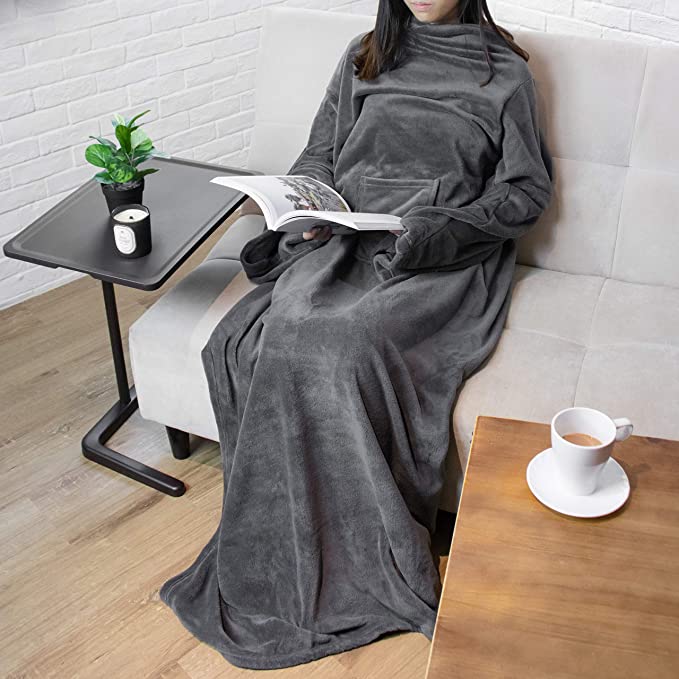 Woman sitting on a couch reading a book while wearing a wearable blanket with sleeves.
