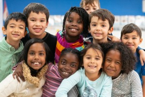 A group of culturally diverse kids stacked on top of each other while cuddling in close and showing how happy they are.
