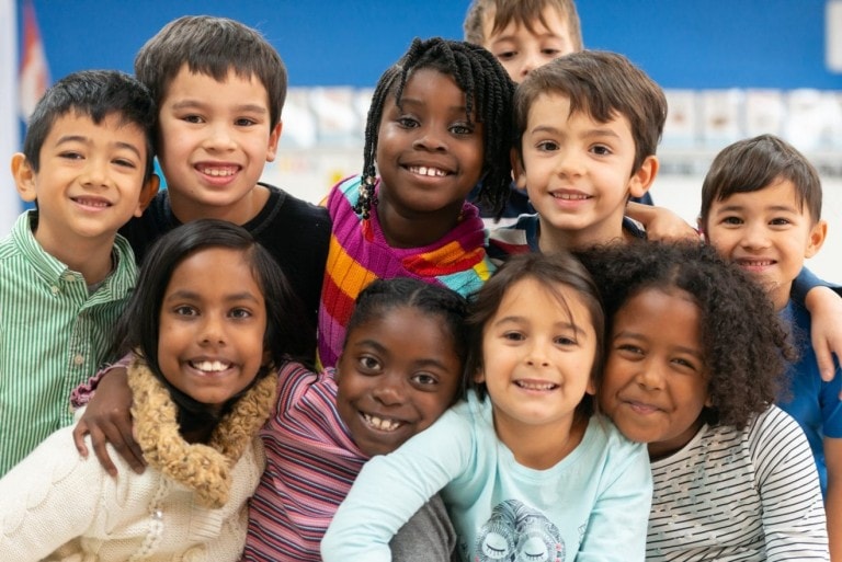 A group of culturally diverse kids stacked on top of each other while cuddling in close and showing how happy they are.