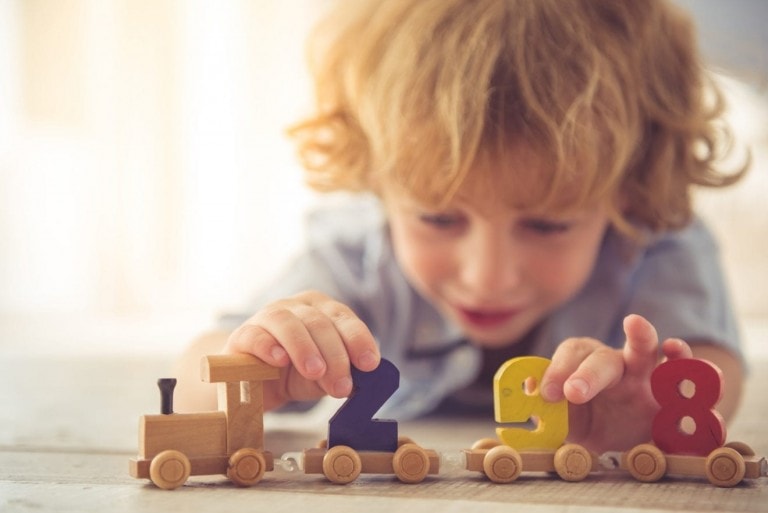 Cute little boy is playing with toy wooden train and numbers at home.