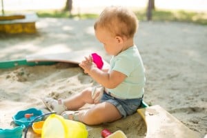 Cute toddler girl playing in sand on outdoor playground. Beautiful baby having fun on sunny warm summer day. Child with colorful sand toys.