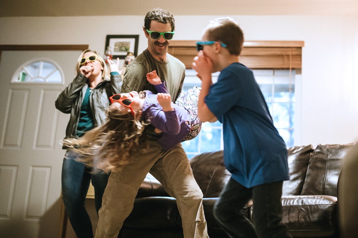 A family has fun being silly and playful in their home, all of them wearing colored sunglasses while they lip synch to their favorite songs and dance around.