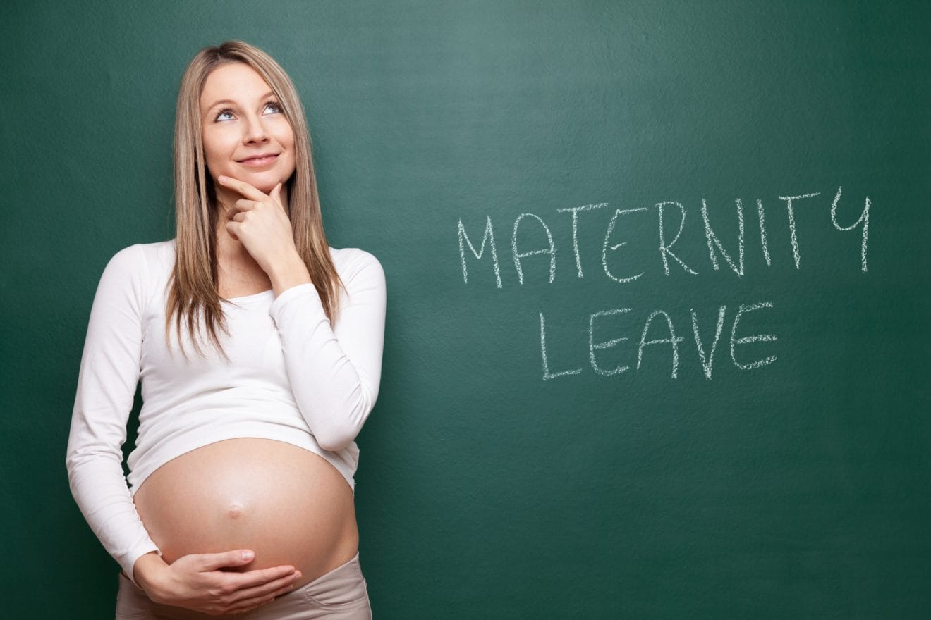 Young pregnant woman and a blackboard behind her that says Maternity Leave