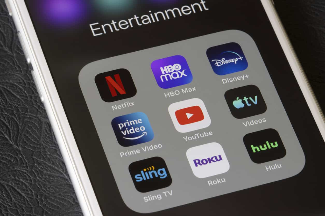 A smartphone screen displaying an Entertainment folder with apps like Netflix, HBO Max, and Hulu rests on a dark textured surface. Perfect for bed rest days, this digital care package offers endless streaming to keep you entertained and relaxed.