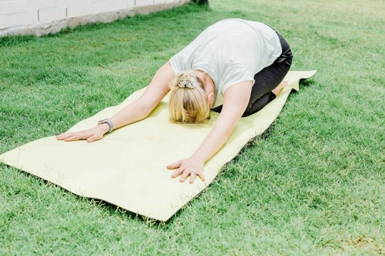 A woman laying on her yoga mat doing child's pose.