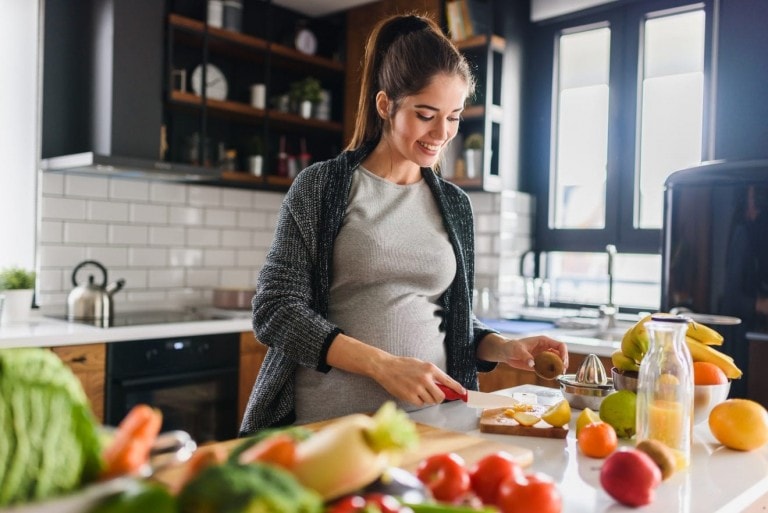 Young beautiful pregnant woman preparing healthy meal with fruits and vegetables.