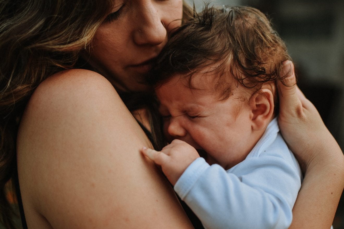 A mother holding her infant child who is crying in her arms.